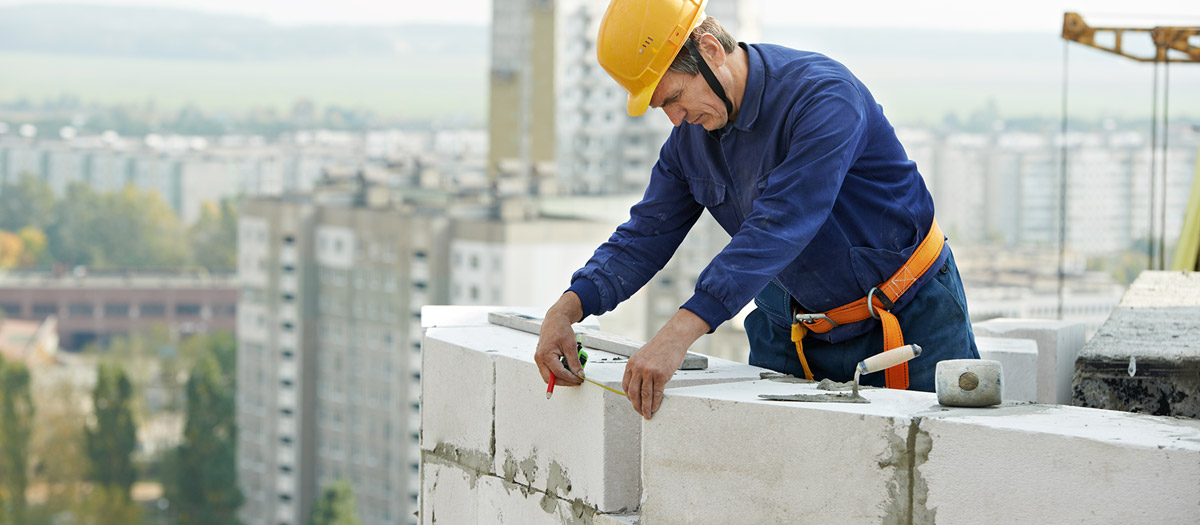 Maon en train de poser des parpaings en haut d'une tour en construction